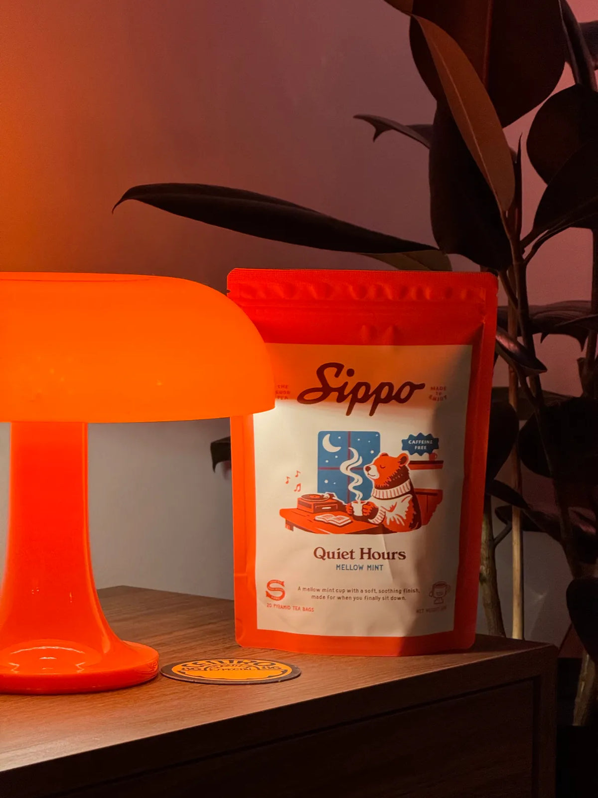 Quiet Hours mellow mint tea pouch lit by a warm orange lamp beside a leafy plant