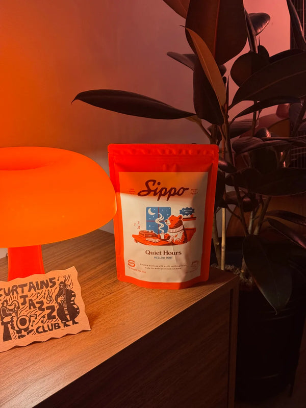 Quiet Hours mellow mint tea pouch on wood beside a glowing lamp and trailing plant